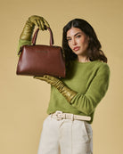 Woman holding a brown handbag against a beige background