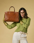 Woman holding a brown crocodile-patterned handbag against a beige background