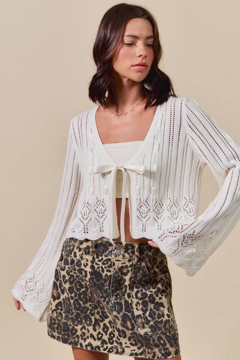 Woman wearing off white pointelle knit tie front cardigan with leopard print skirt
