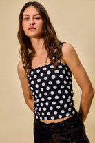 model wearing a black ribbed tank top with white polka dots, featuring a square neckline, wide straps, and a fitted silhouette.