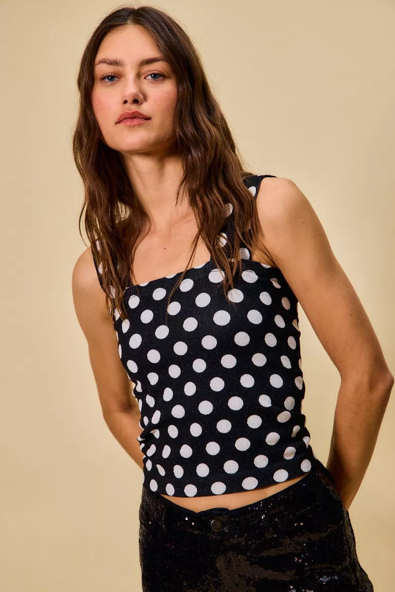model wearing a black ribbed tank top with white polka dots, featuring a square neckline, wide straps, and a fitted silhouette.