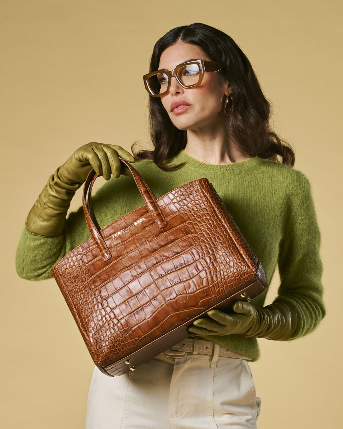 Woman holding a brown crocodile skin handbag against a beige background