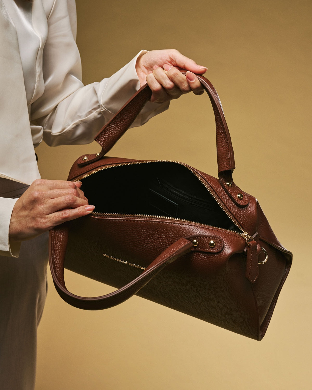 Brown leather handbag held by a person against a beige background