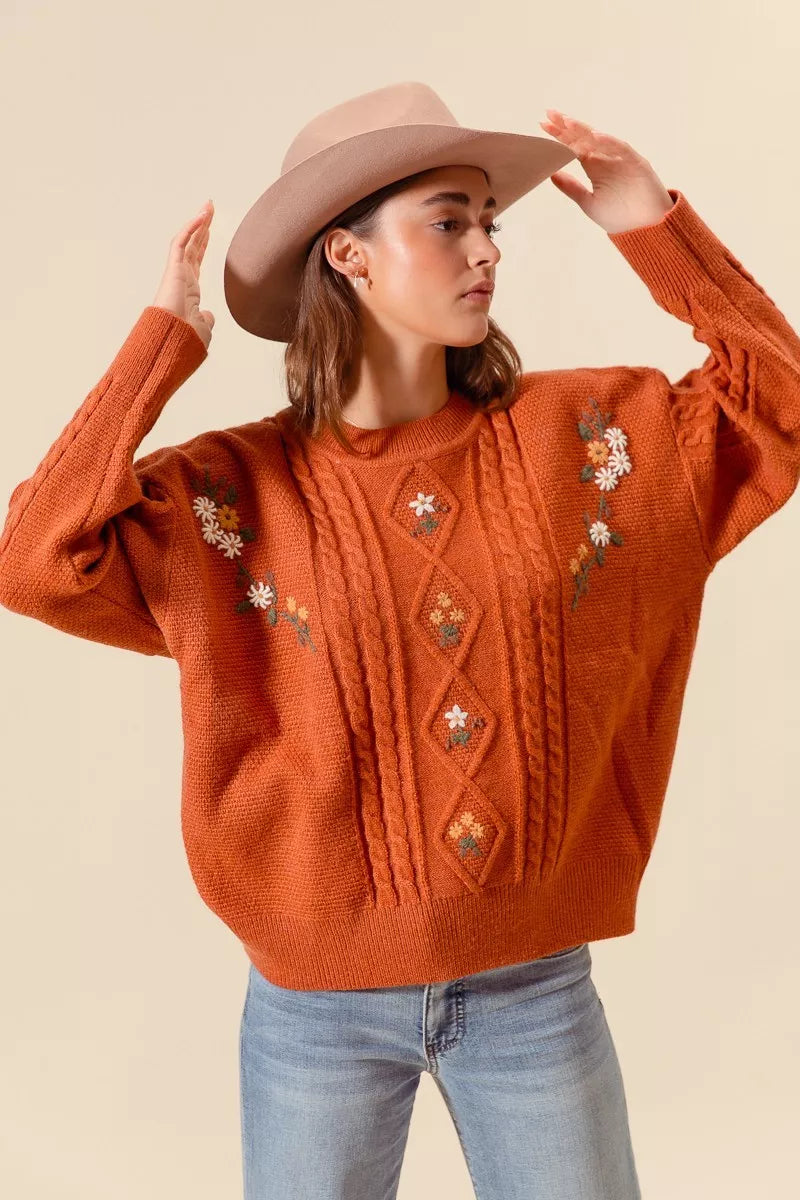 Copper Meadow Floral Knit Sweater in rust orange with embroidered flowers and textured cable detailing, front view.
