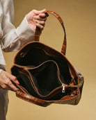 Brown leather handbag held by a person against a beige background