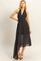 Black halter midi dress featuring an asymmetrical handkerchief hem and fabric rosette detail at the hip.