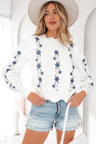 Close-up front view of ivory sweater with navy floral embroidery details
