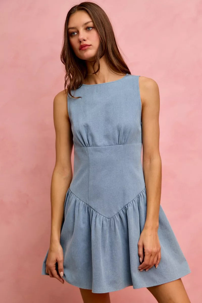 Sleeveless soft denim mini dress with boat neckline, fitted bodice, drop waist seam, gathered skirt, and flared silhouette