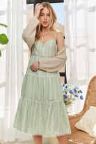 Woman styling a sage gingham midi dress with a neutral knit cardigan for an elevated daytime look.