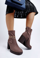 Brown ankle boots styled with gold chain and black velvet skirt with blue bag on a white background