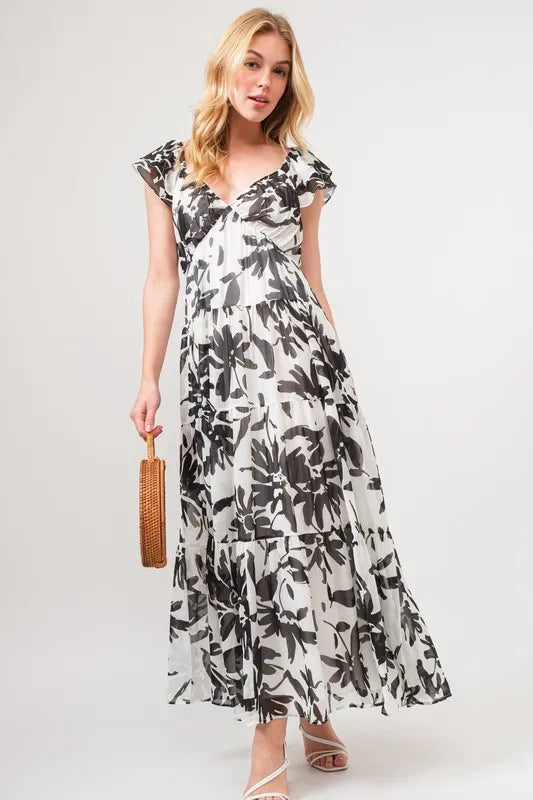 Model wearing a black and ivory floral tiered maxi dress with flutter sleeves and flowing silhouette | AVAH Collections
