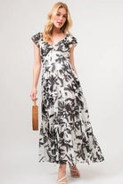 Model wearing a black and ivory floral tiered maxi dress with flutter sleeves and flowing silhouette | AVAH Collections
