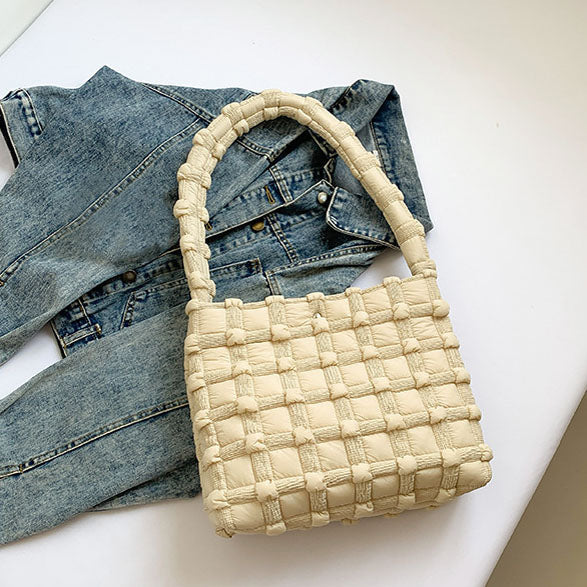 Beige basket weave puff tote bag on a white surface with denim jeans