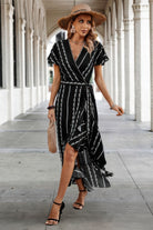 Woman in a black and white patterned dress with a straw hat walking on a stone pathway.