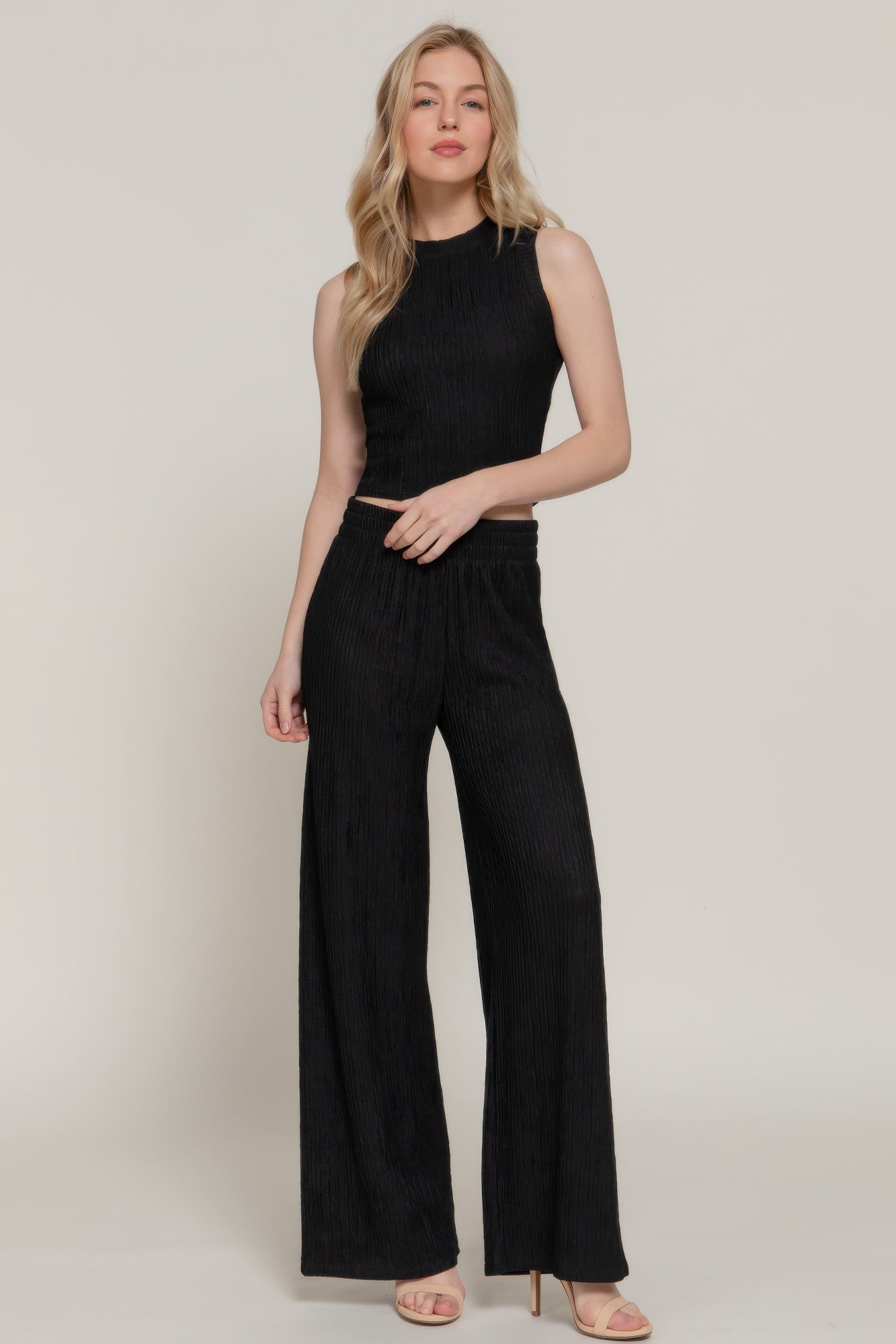 Model wearing a black sleeveless top and wide-leg pants on a plain background