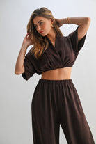 Model in brown lounge set with arms raised, highlighting draped collar and waistline.