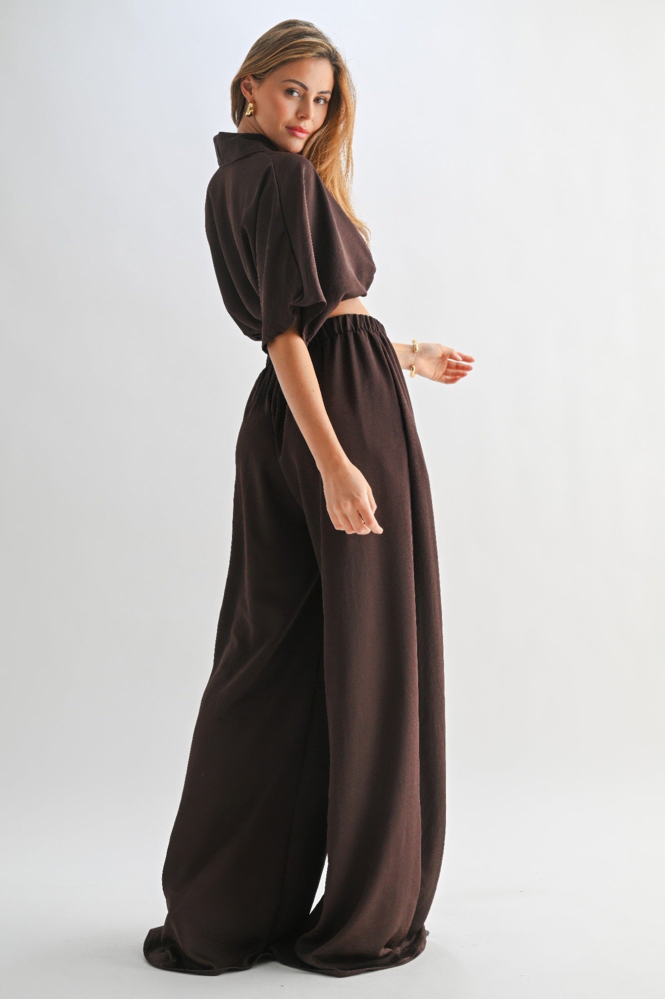 Side profile view of model wearing chocolate shawl collar crop top and wide-leg pants.