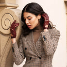 Woman wearing a checkered coat and maroon gloves against a neutral background