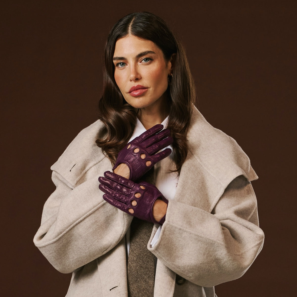 Woman wearing a beige coat and purple gloves against a brown background
