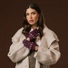 Woman wearing a beige coat and purple gloves against a brown background