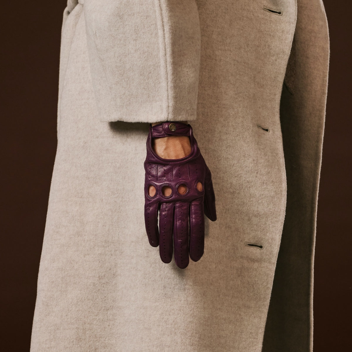 Purple leather glove on a person wearing a beige coat against a dark background