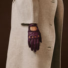 Purple leather glove on a person wearing a beige coat against a dark background