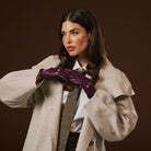 Woman wearing a beige coat and purple gloves against a brown background