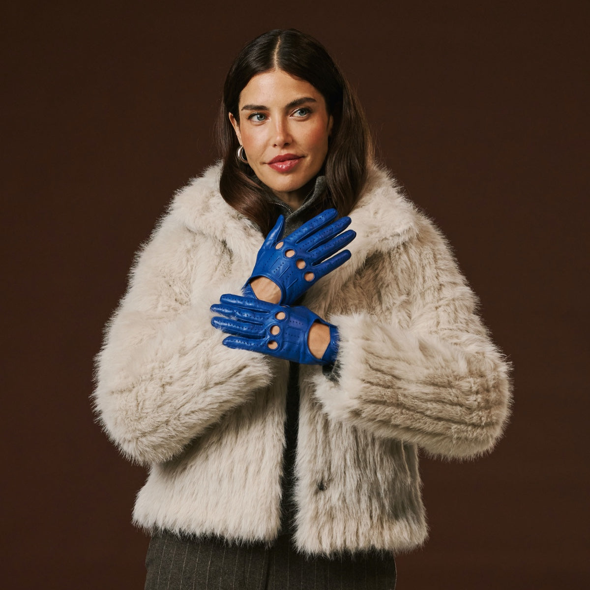 Woman wearing a beige fur coat and blue leather gloves against a brown background