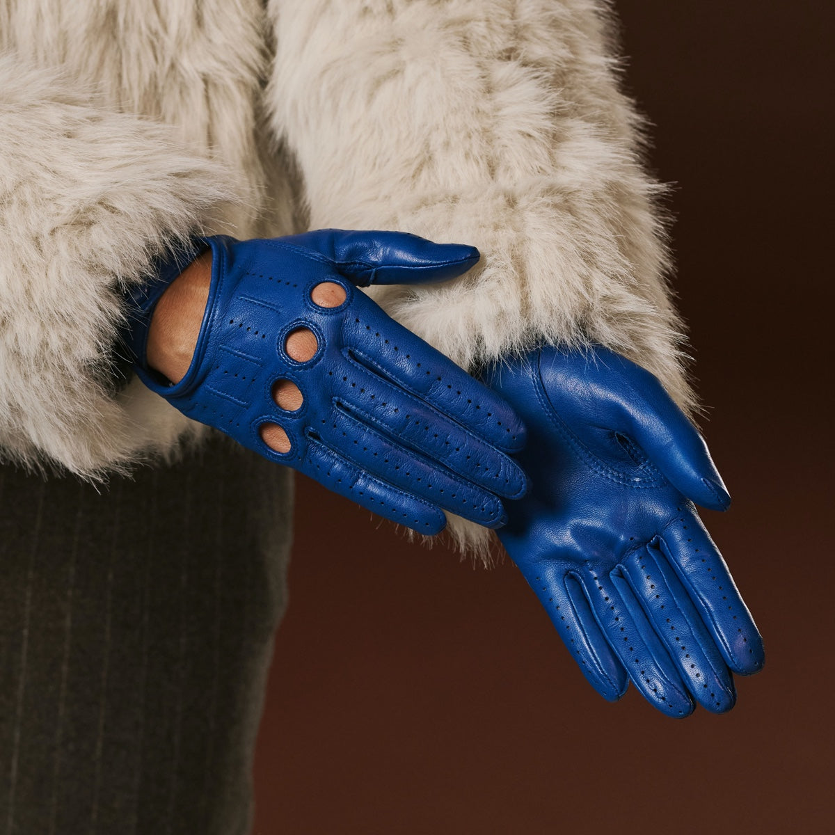 Blue leather gloves worn with a fur-lined coat on a brown background