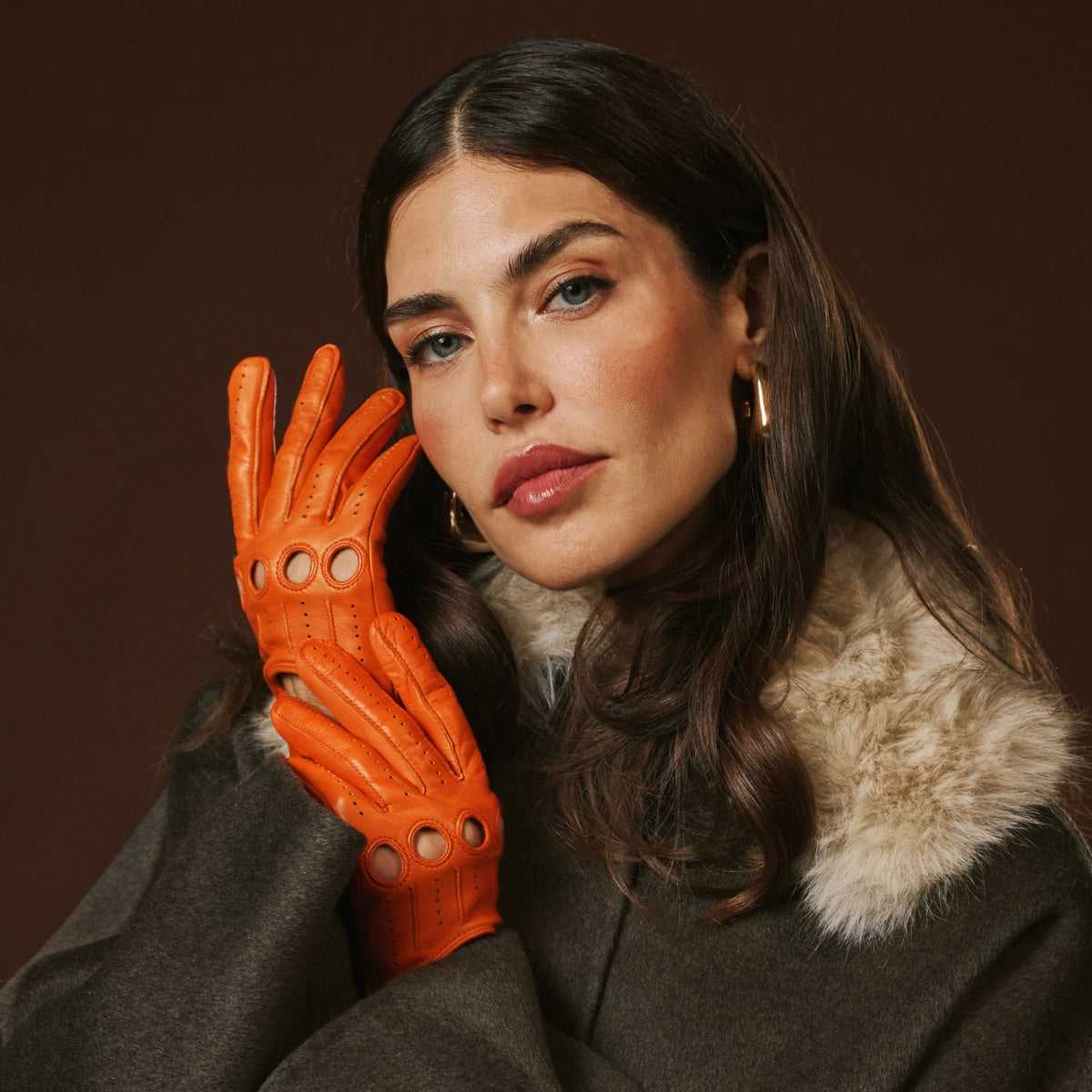 Woman wearing an orange leather glove against a brown background