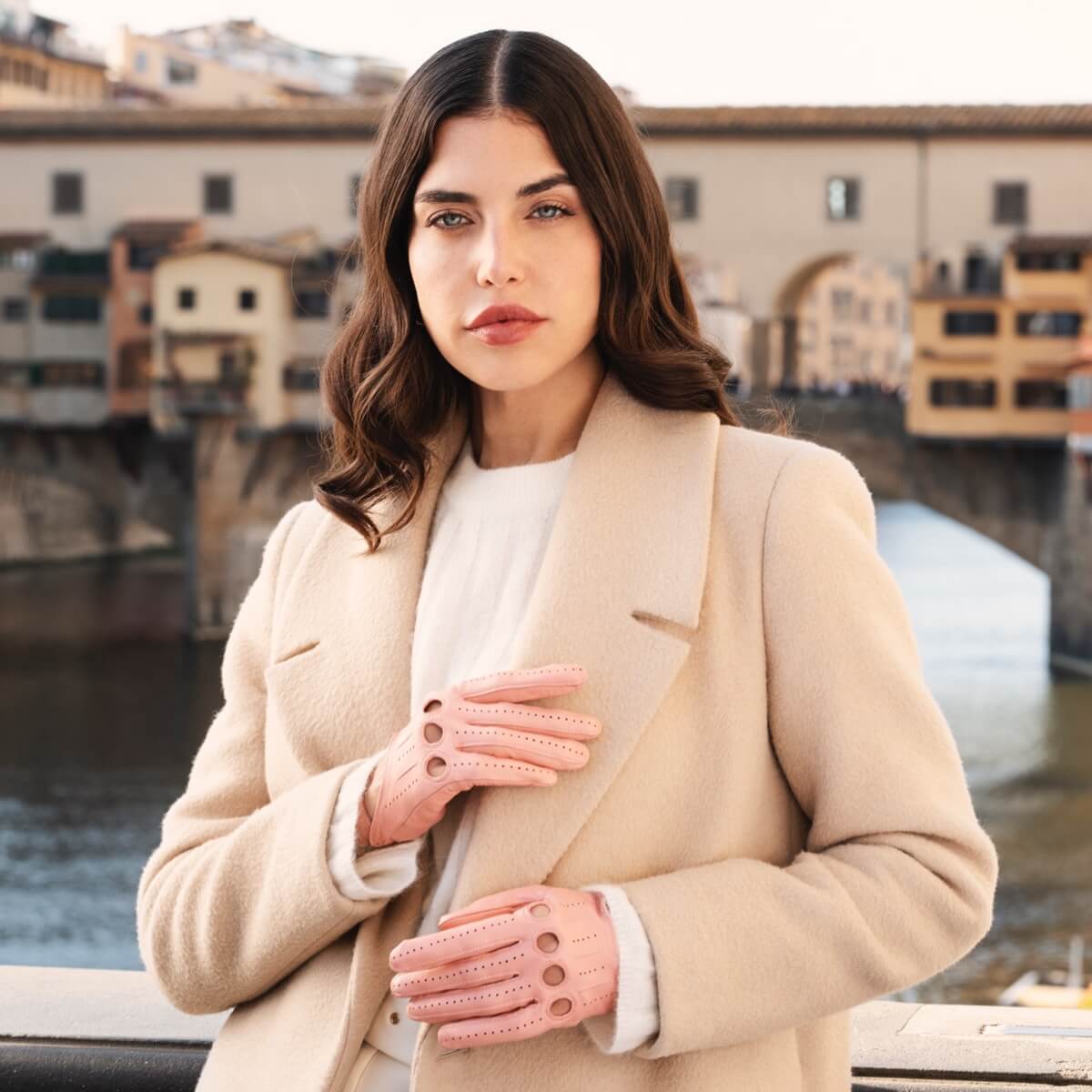 Woman wearing a beige coat and pink gloves with a blurred cityscape background
