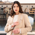 Woman wearing a beige coat and pink gloves with a blurred cityscape background