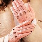 Pink leather gloves with cut-out design worn by a person in a beige coat.