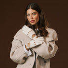 Woman wearing a beige coat and white leather gloves against a brown background