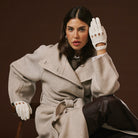 Woman wearing a beige coat and white leather gloves against a brown background