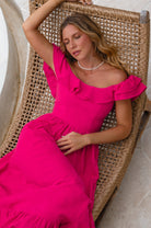 Woman in a bright pink midi dress with oval neckline and smocked and ruffled off-the-shoulder sleeves lounging in a wicker chair