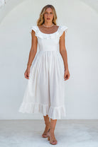 Woman in a white midi dress with oval neckline and smocked and ruffled off-the-shoulder sleeves against a white background, front view