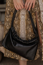 Black mini leather handbag held by a person wearing a patterned dress.