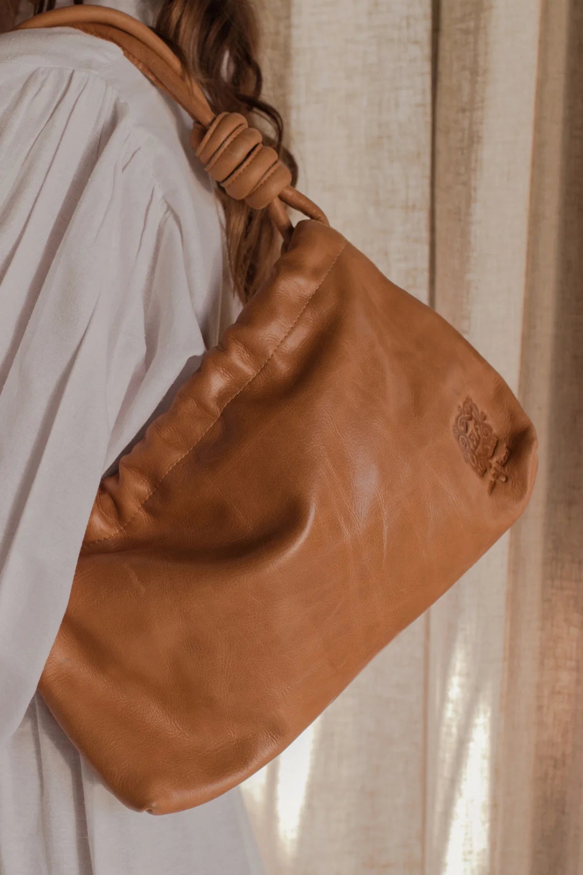 Tan leather bag held by a person with a neutral background