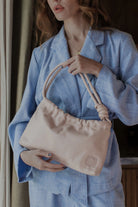 Person holding a beige leather handbag with a brand logo, wearing a blue outfit.
