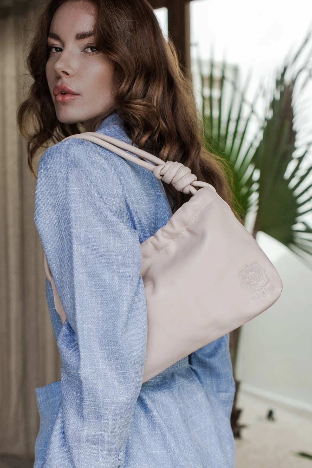 Woman wearing a light blue shirt with a beige handbag, outdoor setting