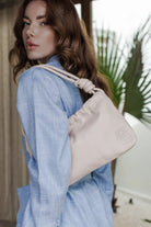 Woman wearing a light blue shirt with a beige handbag, outdoor setting
