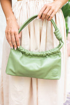 Green handbag held by a person wearing a light-colored dress.