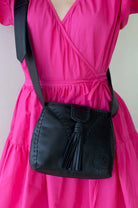Black handbag with a tassel detail worn by a person in a bright pink dress.