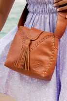 Camel leather handbag with fringe details and wide crossbody strap worn by person in purple
