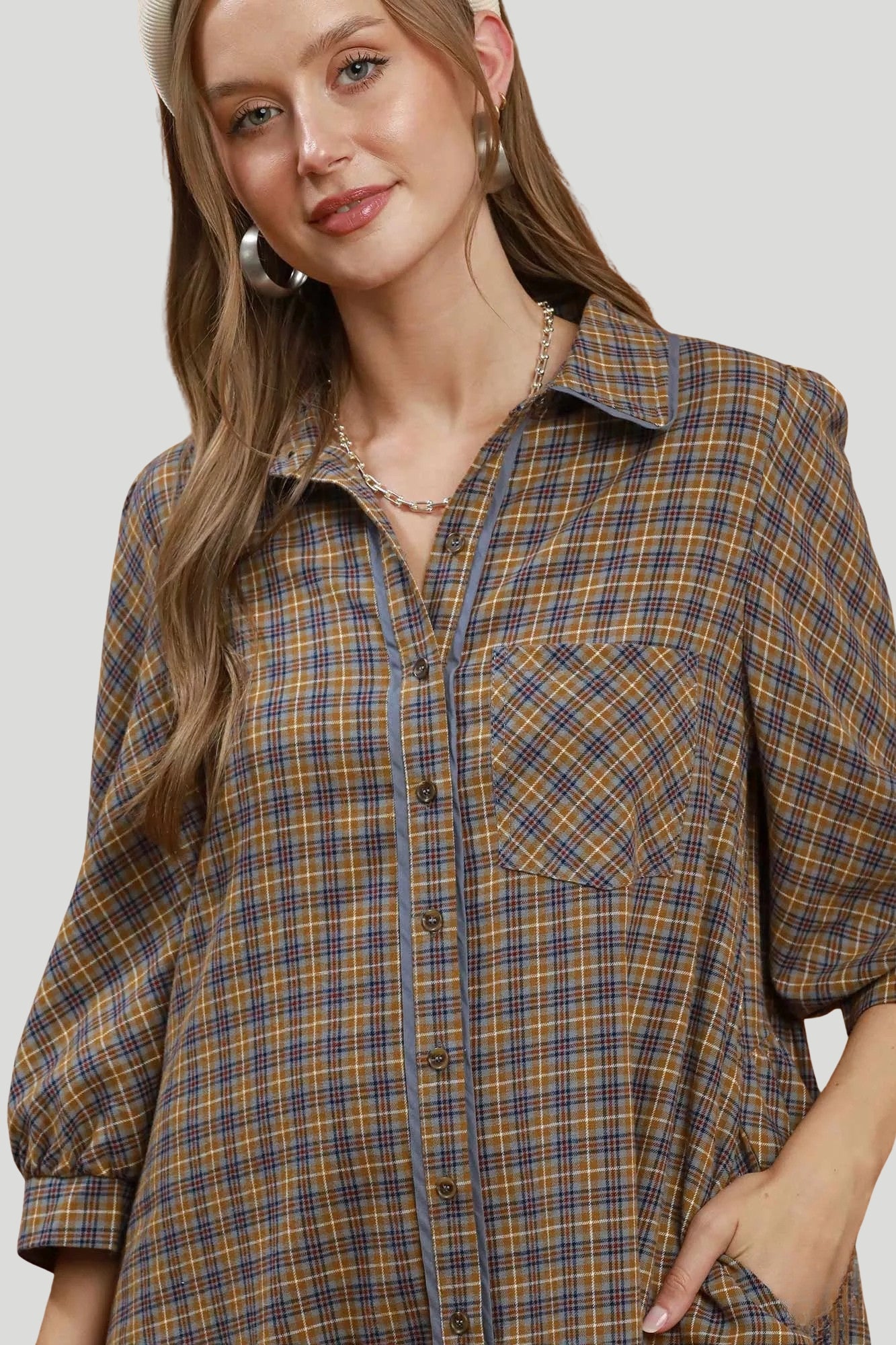 Close up of brown and grey plaid shirt dress showing collared neckline, contrast piping, buttons and chest pocket.