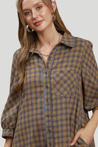 Close up of brown and grey plaid shirt dress showing collared neckline, contrast piping, buttons and chest pocket.