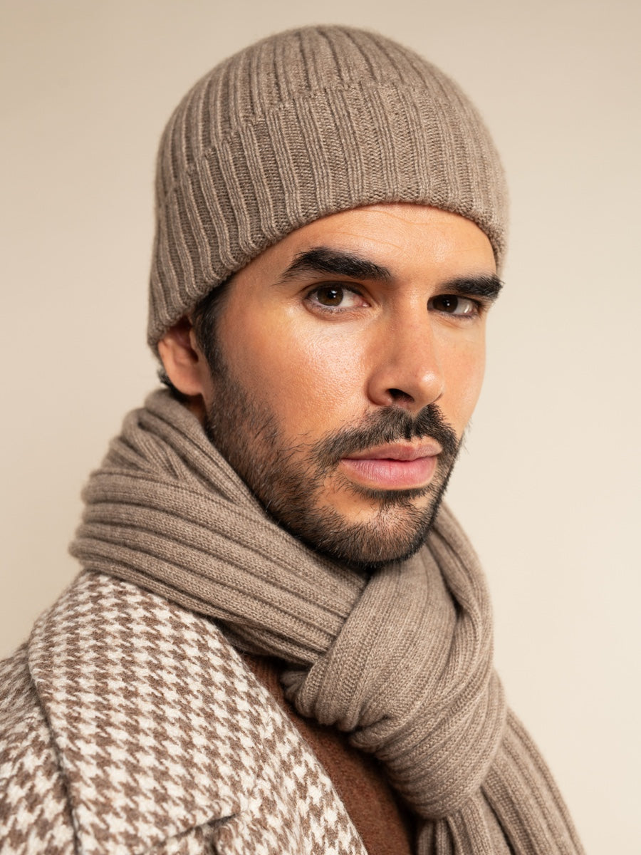Man wearing a beige knit beanie and scarf against a plain background
