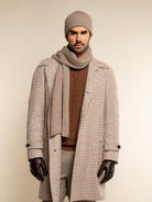 Man wearing a checkered coat, brown sweater, scarf, beanie, and gloves on a beige background