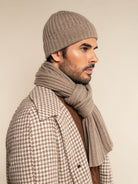 Man wearing a patterned coat, beanie, and scarf against a beige background